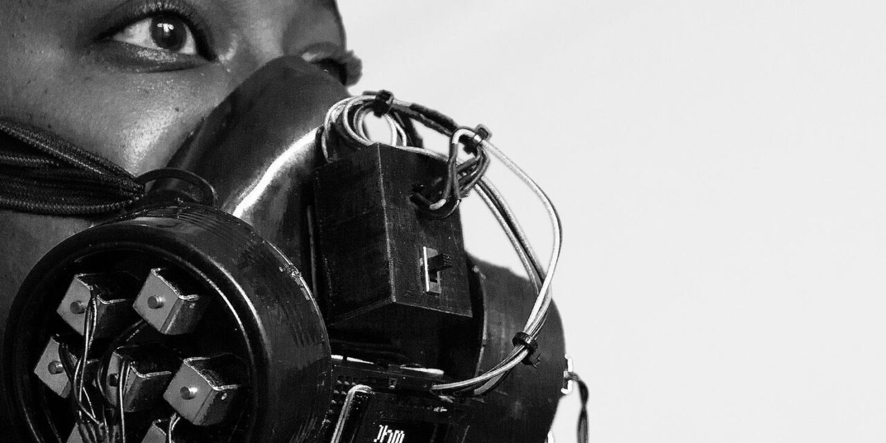 Black and white close-up of a person with a gas-mask-type contraption in front of a microphone.