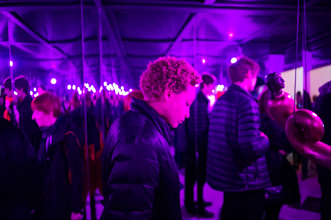 A woman, dressed in purple light, gazes downward in a reflective, purple room.